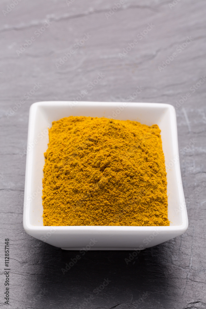 Curry Pulver in weißer Schale auf dunkler Schieferplatte. Curry Pulver in weißer Schale auf dunkler Schieferplatte.