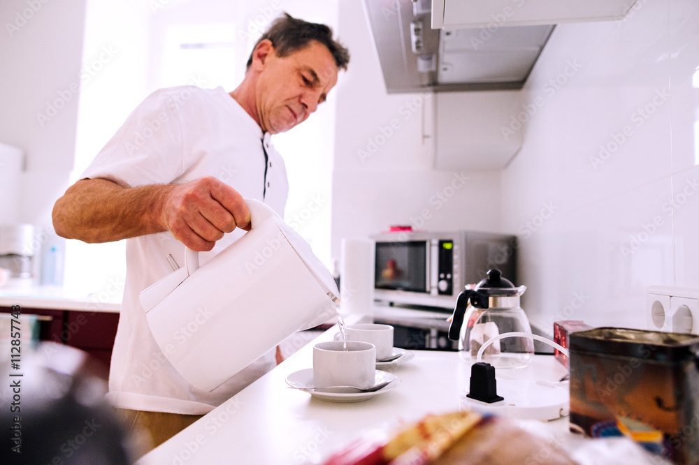 Senior man preparing coffee. Pouring water into a cup.