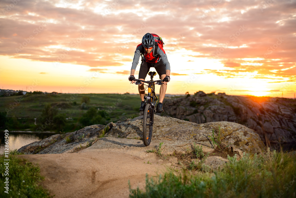 Fototapeta premium Cyclist Riding the Bike on the Mountain Rocky Trail at Sunset