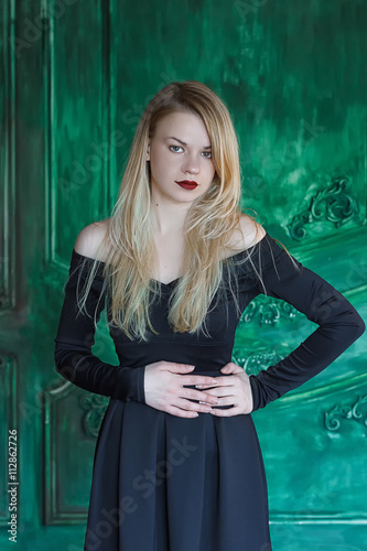 Elegant blonde in a black dress near grunge wall