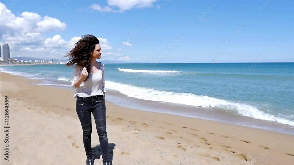 Happy young woman with beautiful curly hair walking on the sea beach, slow motion Happy young woman with beautiful curly hair walking on the sea beach, slow motion
