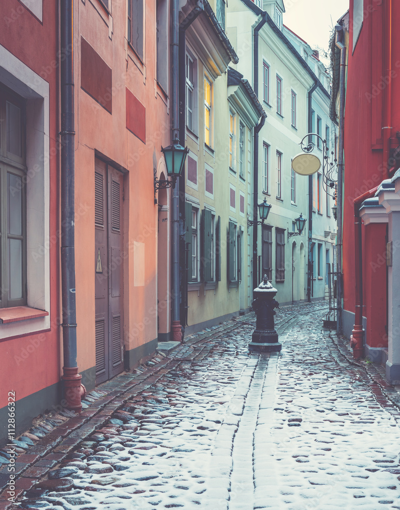 Obraz premium Wintry motif with narrow medieval street in old Riga city. Riga is the capital and largest city of Latvia, a major commercial, cultural, historical and financial center of the Baltic region