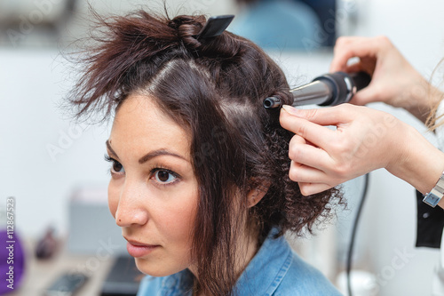 Woman hairdresser making hairstyle using curling iron for long 