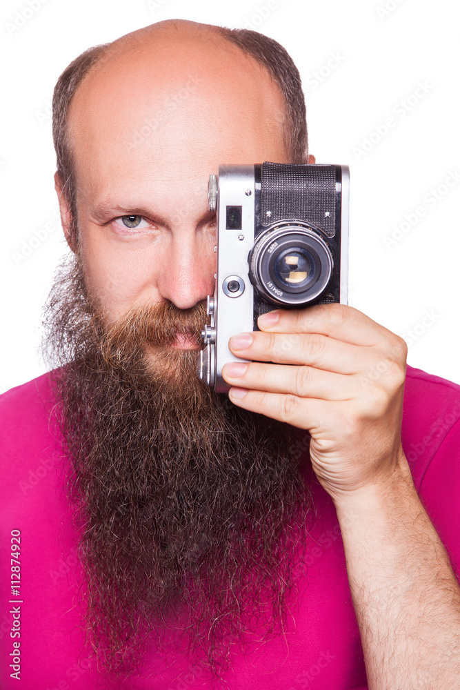 The portrait of bald bearded man photographer with pink t shirt holding classic camera. isolated on white background. studio shot. The portrait of bald bearded man photographer with pink t shirt holding classic camera. isolated on white background. studio shot.