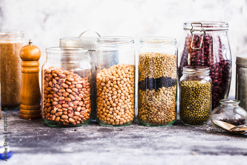 Collection of grain products, lentils, soybeans and red beans in storage jars over on kitchen rural table. Collection of grain products, lentils, soybeans and red beans in storage jars over on kitchen rural table.