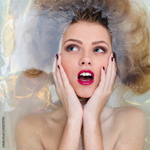 closeup on elegant pinup girl with silk skin, excellent blond hair, mouth open in pleasure having fun happy relaxing laying in clear water on copy space background portrait