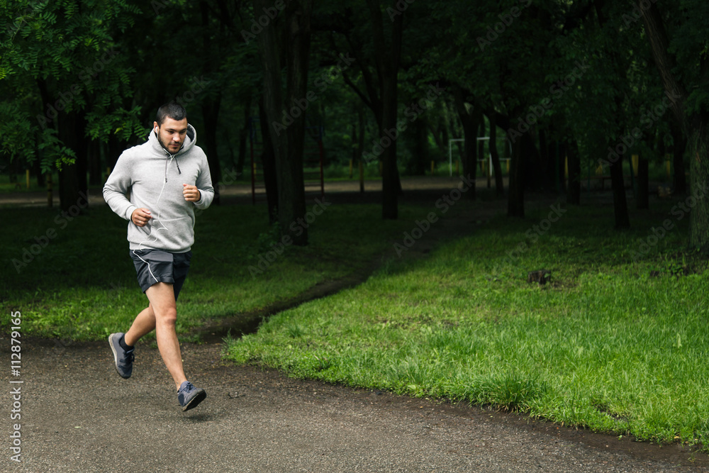 young man in sportswear running in the early morning in the Park and listening to music young man in sportswear running in the early morning in the Park and listening to music