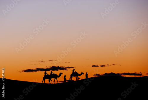 A small group of tourists during a camel trekking at sunset on the sand dunes of Erg Chebbi, Morocco