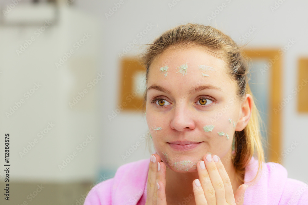 Woman cleaning her face with scrub in bathroom. Woman cleaning her face with scrub in bathroom.