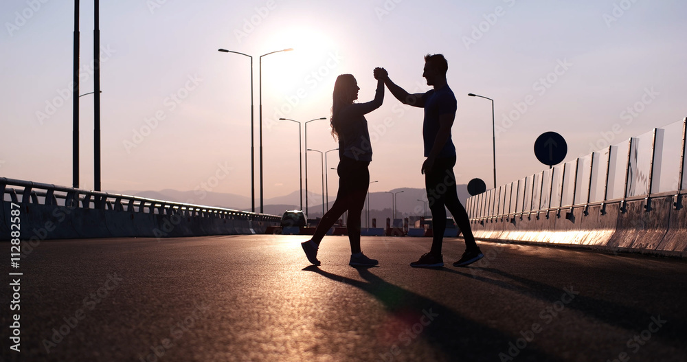Silhouette of a fitness couple profile stretching at sunset with