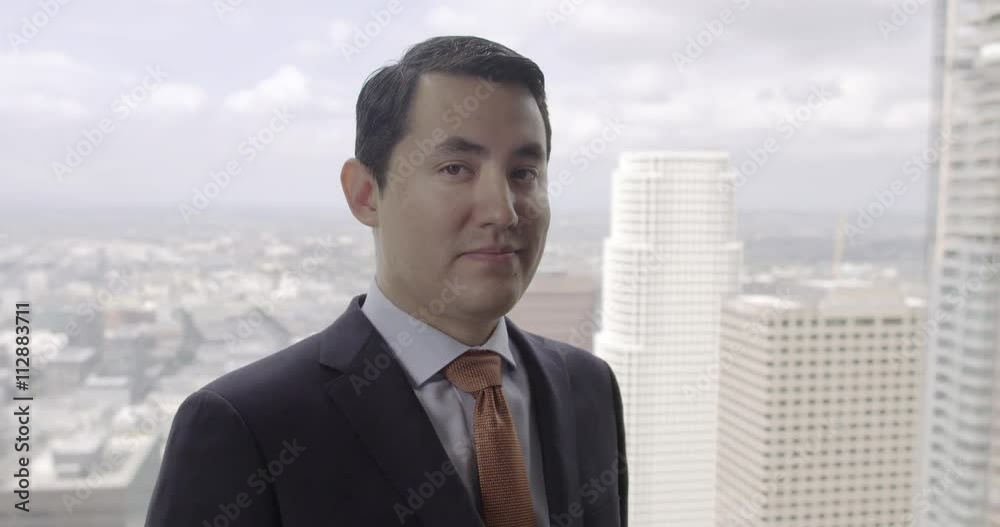 Successful young business man in suit and tie stands in front of a skyscraper window with views across Los Angeles. Medium close up, front view, dolly shot originally recorded in 4K Successful young business man in suit and tie stands in front of a skyscraper window with views across Los Angeles. Medium close up, front view, dolly shot originally recorded in 4K
