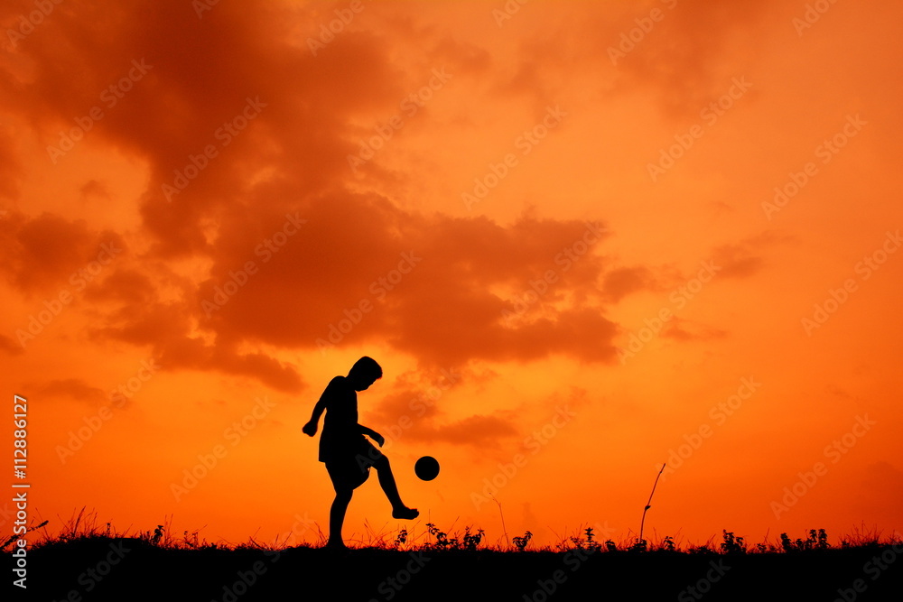 Silhouette a boy playing football in the sunset