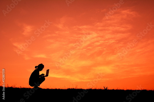 Silhouette women using computer at sunset