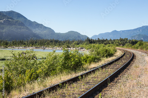 Rail tracks by a swampy lake surounded by mountains. Taken in Squamish, British Columbia, Canada on a sunny day.