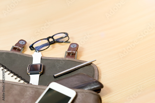 Outfit of traveler on wooden background: leather bag, smartwatch,smartphone, glasses, notebook and pen top view . retro style ,vintage tone
