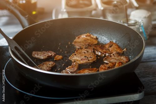 Pieces of meat on pan. Frying pan with brown meat. Veal medallions with whole pepper. Preparation of high-calorie dish.