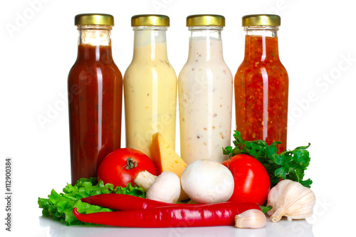Fototapeta Naklejka Na Ścianę i Meble -  a variety of sauces in glass bottles with vegetables and spices on a white isolated background
