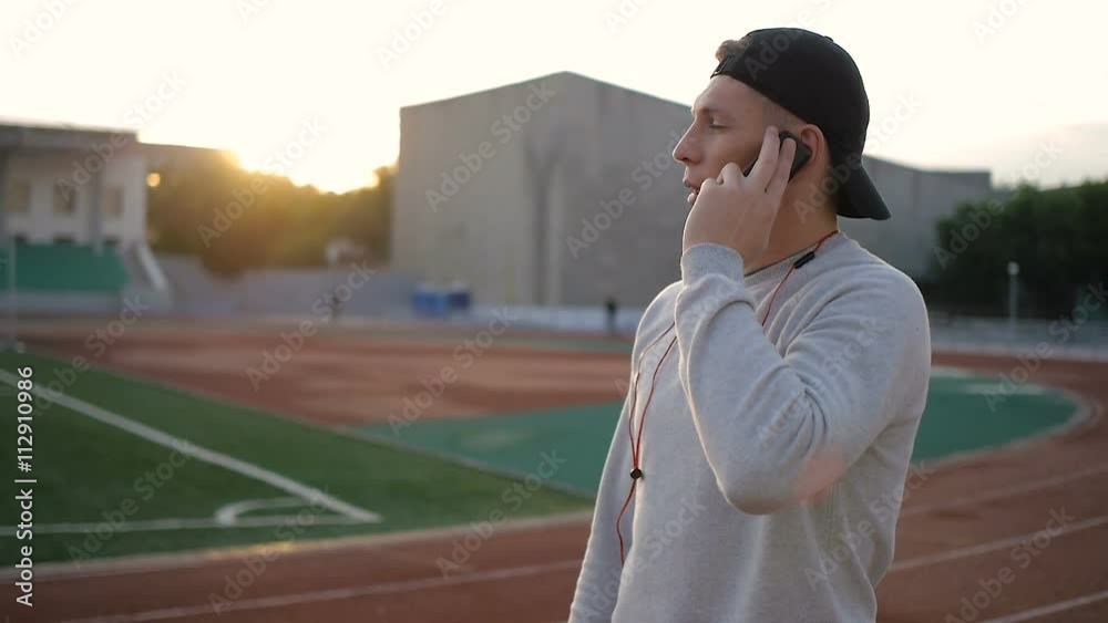 young fitness man talks on the phone on stadium track in slow motion young fitness man talks on the phone on stadium track in slow motion