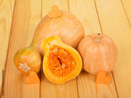 Fresh ripe pumpkin and half against backdrop of pale wood.