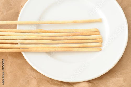 grissini su un piatto bianco, vista dall'alto con sfondo di carta marrone.