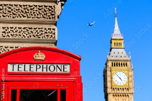 Iconic red telephone box with Big Ben and a passing flight against blue sky in the background