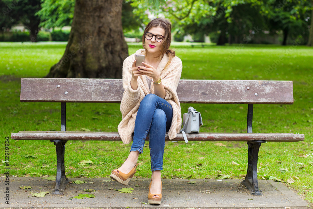 Cute young girl sitting on the bench and using smartphone in the park Cute young girl sitting on the bench and using smartphone in the park