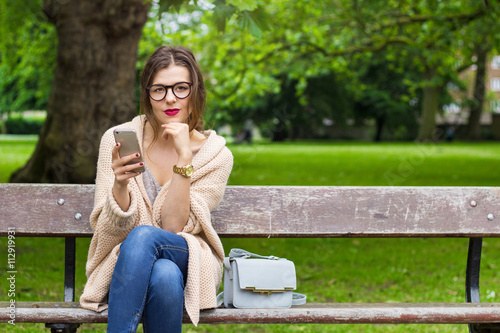Young woman sitting in the park with phone  © maryanski