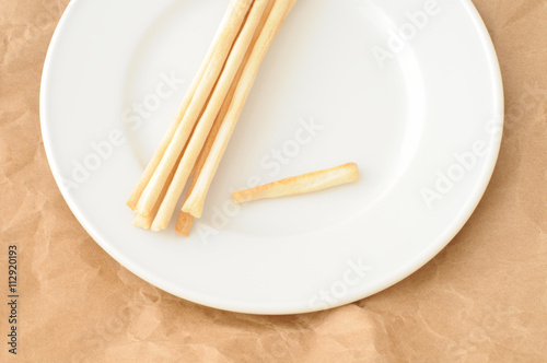 grissini, tipo fine, su un piattino bianco, sfondo di carta marrone, vista dall'alto