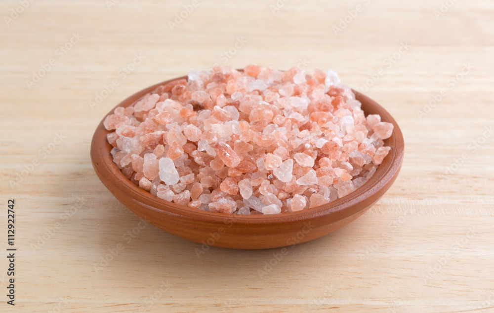 Side view of Himalayan pink salt in a small bowl on a wood table. Side view of Himalayan pink salt in a small bowl on a wood table.