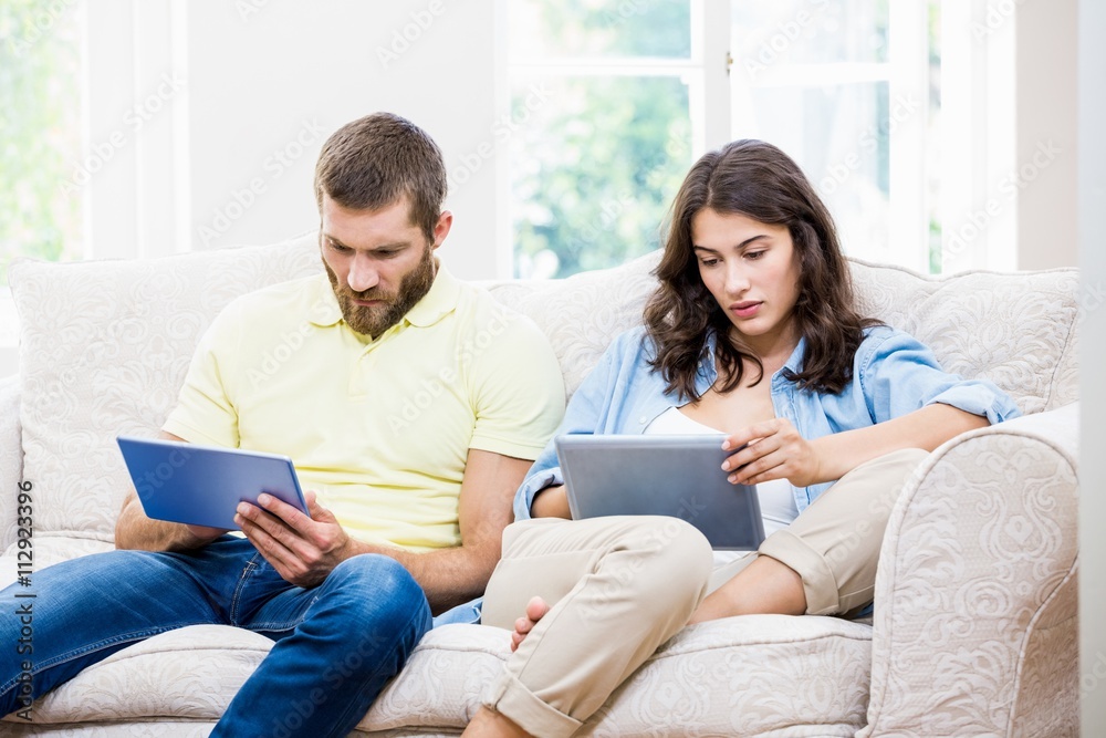 Couple sitting on sofa and using digital tablet in living room Couple sitting on sofa and using digital tablet in living room
