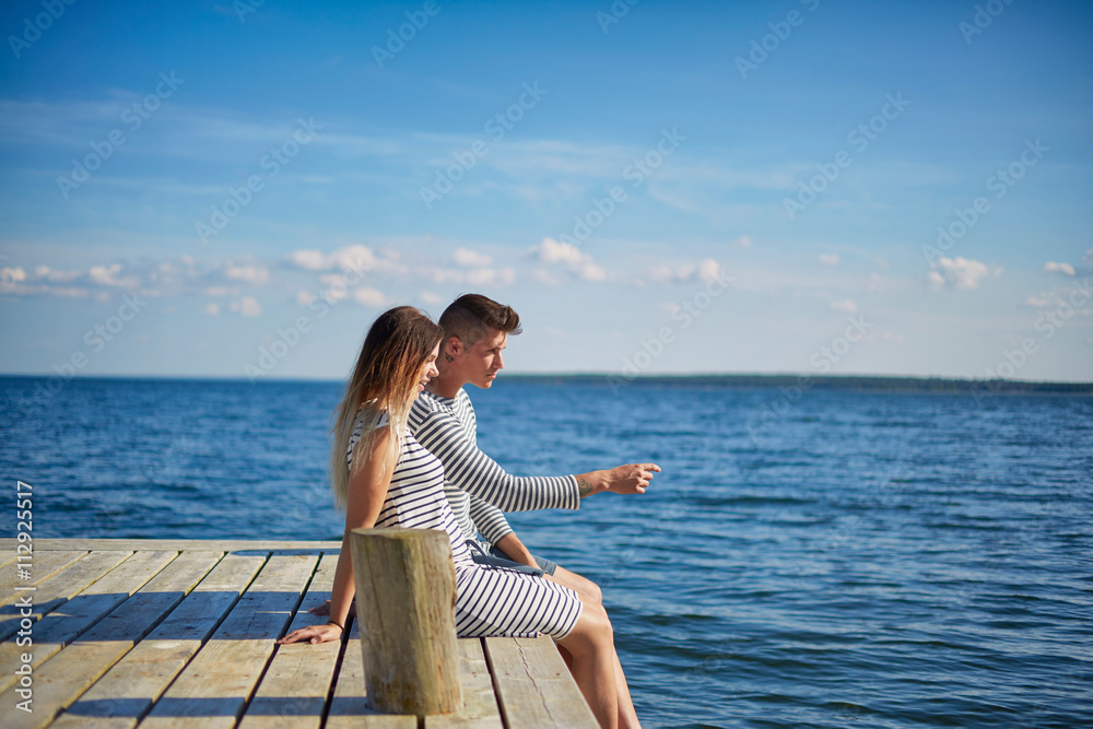 Couple sitting on wooden pier, looking at view Couple sitting on wooden pier, looking at view