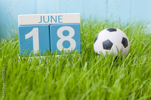 June 18th. Image of june 18 wooden color calendar on green grass background with football outfit. Summer day