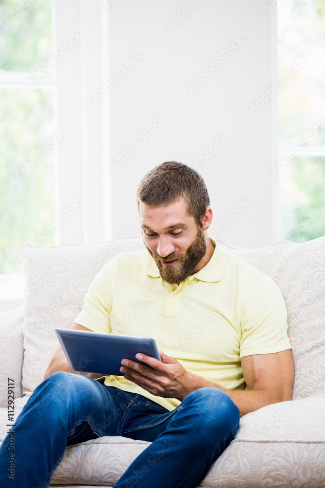 Young man sitting on sofa and using digital tablet