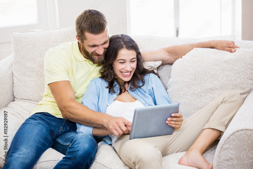 Couple sitting on sofa and using digital tablet in living room