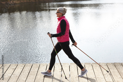Full length side view of woman nordic walking by pond