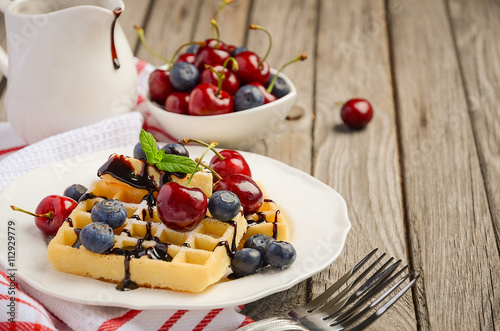 Waffles with chocolate sauce, cherries and blueberries, selective focus, copy space