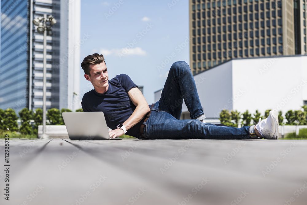 Young man lying outdoors using laptop Young man lying outdoors using laptop