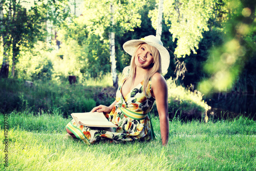 Blonde young woman girl with hat relaxing in a park reading book, sitting alone on grass photo