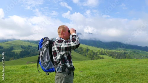 4K.Tourist  man backpacker in mountains looks in binoculars.