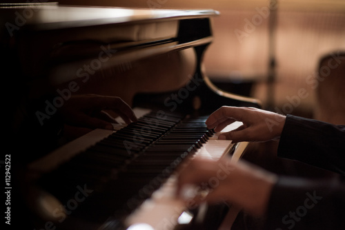 Hands of young man playing piano keys in bar at night photo