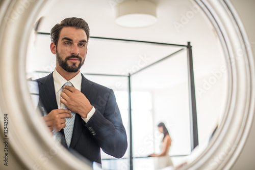 Mirror reflection of young businessman adjusting shirt and tie in hotel room, Dubai, United Arab Emirates