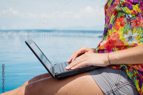 Smiling freelancer sitting by pool with laptop.