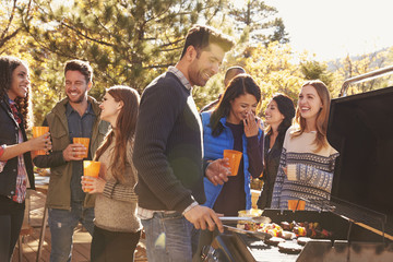 Group of friends stand at a barbecue, one cooking at grill
