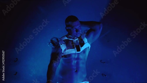 Muscular sexy naked man dancing in the studio on blue light background