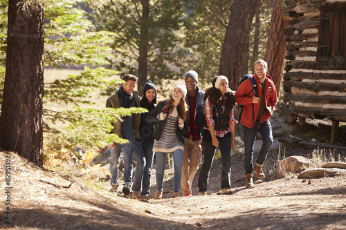Six friends walking on forest path past a log cabin © Monkey Business