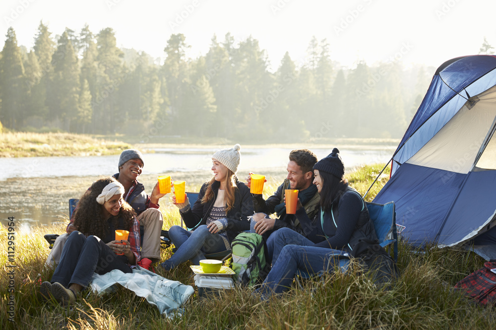 Group of friends drinking outside their tent near a lake