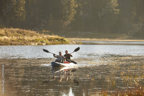 Two young men kayaking on a lake, forest in background