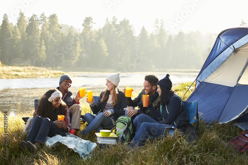 Group of friends drinking outside their tent near a lake