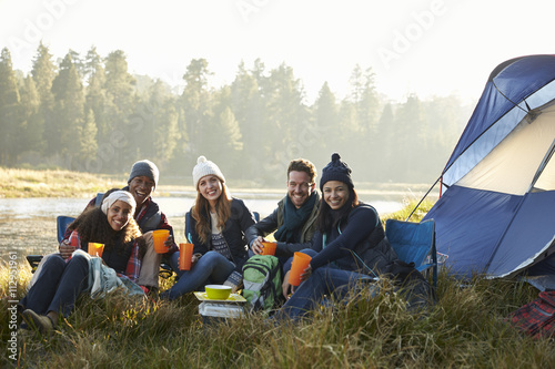 Friends sitting outside a tent near a lake looking to camera