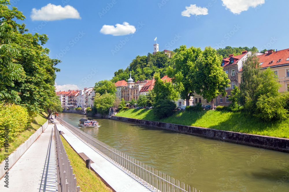 Fototapeta premium Boat on Ljubljanica river and castle raising above on the hilltop, Ljubljana, Slovenia